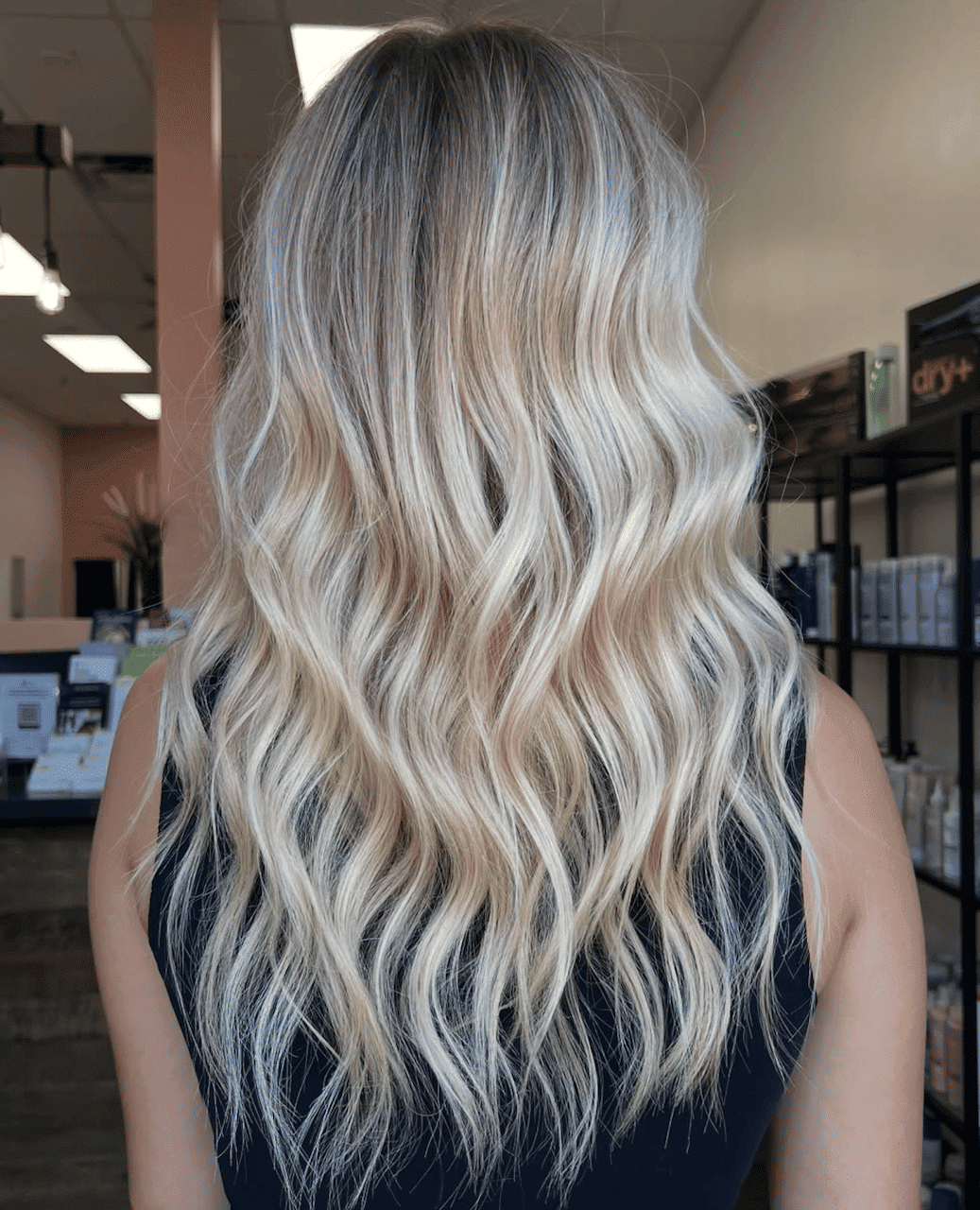 Wavy blonde hairstyle on a person in a salon setting.