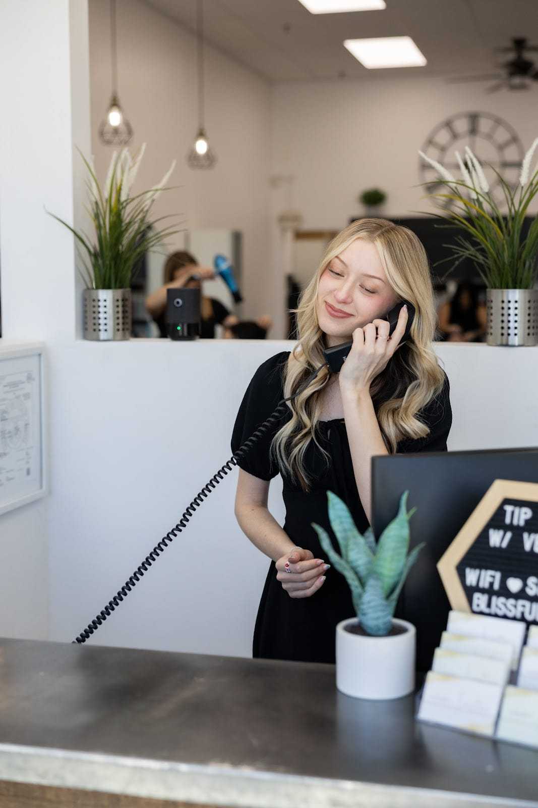Receptionist answering a phone at a modern, plant-decorated front desk.