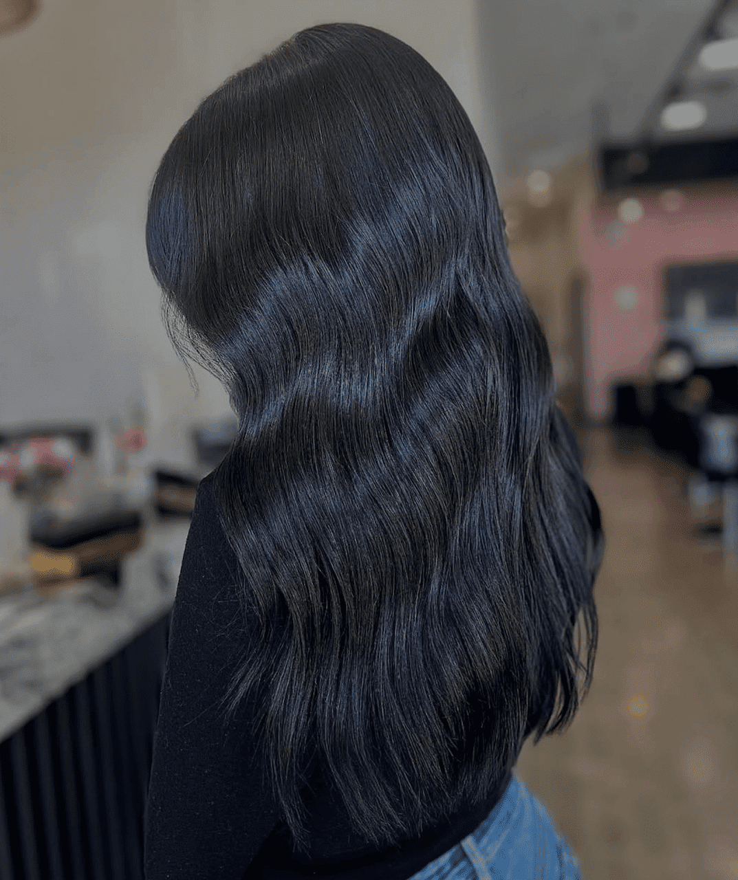 Wavy black hair cascading down a woman's back in a salon setting.