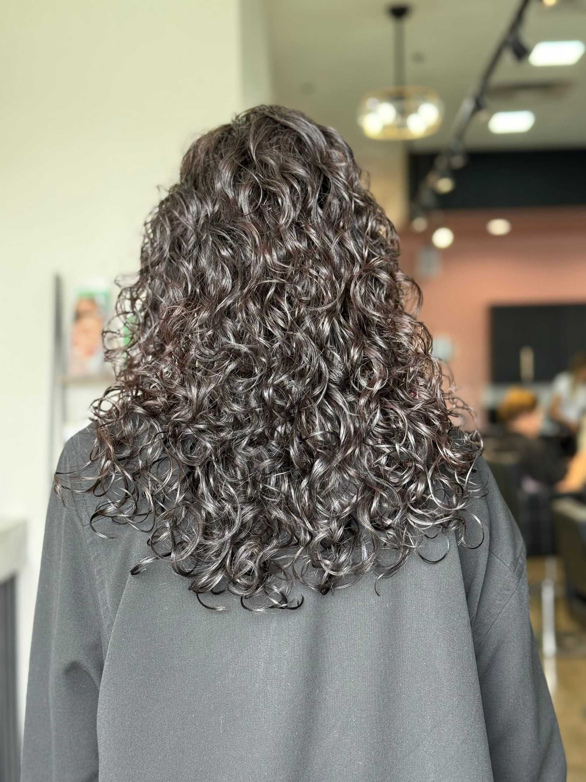 Curly hairstyle with glossy, well-defined ringlets in a salon setting.